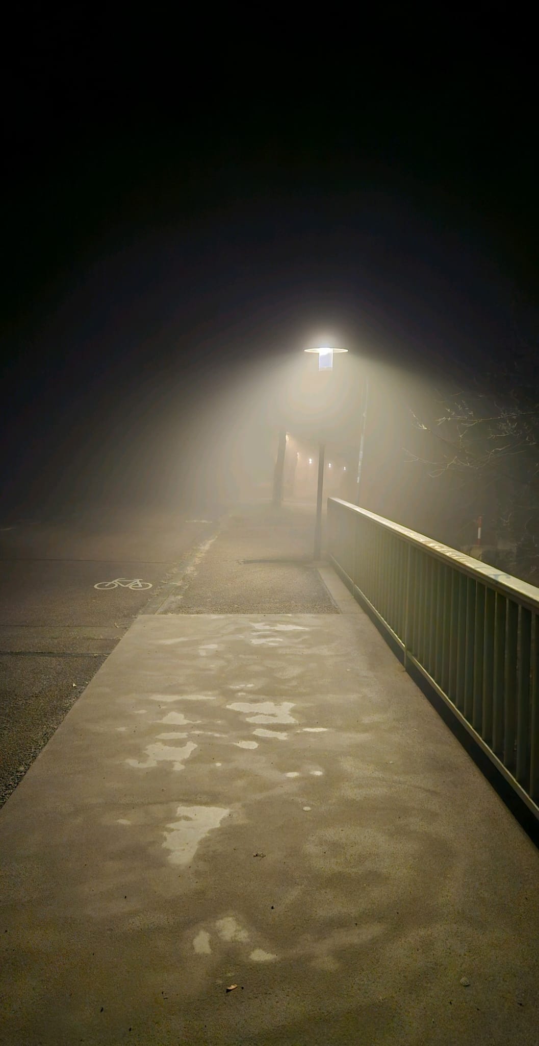 Nebliger Weg bei Nacht mit leuchtender Straßenlaterne und Brückengeländer